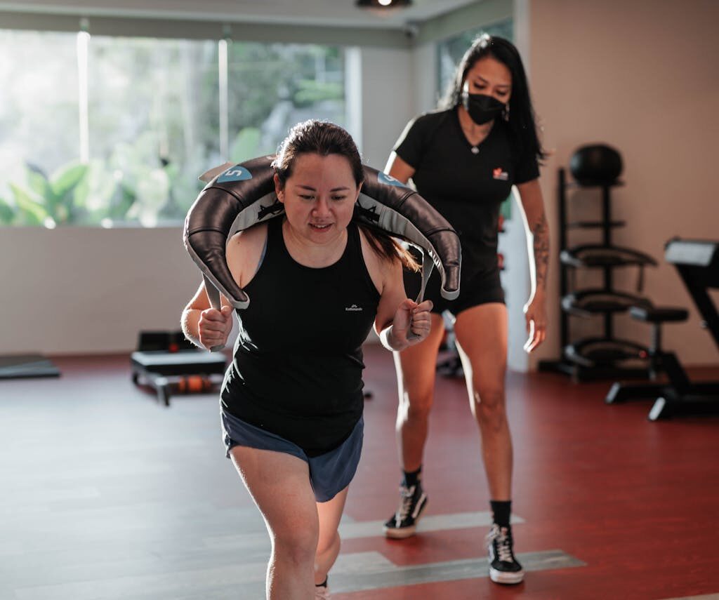 Two women focused on strength training in a Singapore gym with a personal trainer.