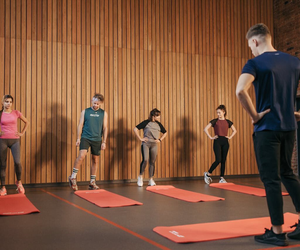A group exercise class with a personal trainer leading stretching exercises in a gym.