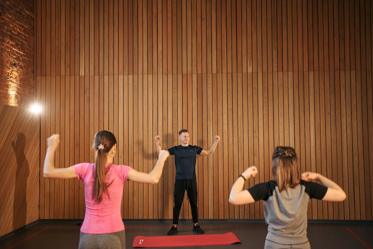 Instructor guiding two women in a gym workout session. Indoor fitness training.